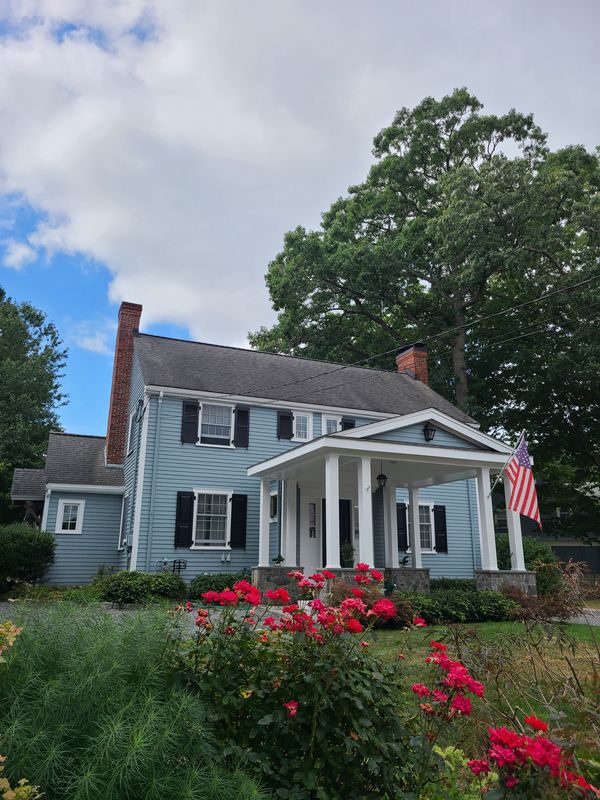 Pale blue colonial with black shutters and columned portico after repainting