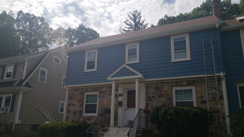 Blue colonial with fieldstone facade during exterior work