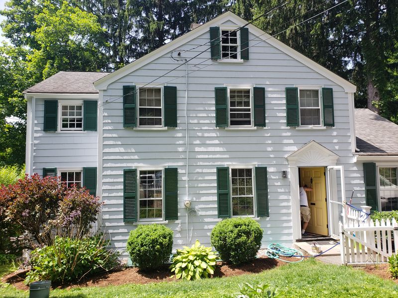 Colonial exterior with dark green shutters during repainting
