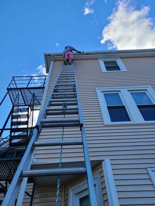Aura Painting crew member working a third-floor elevation from an extension ladder