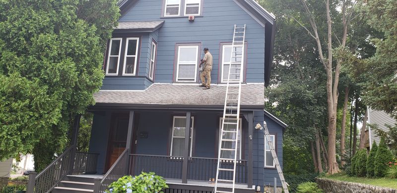 Painter working from a porch roof on a Victorian exterior