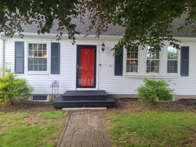 White cape with black shutters and red door after exterior work